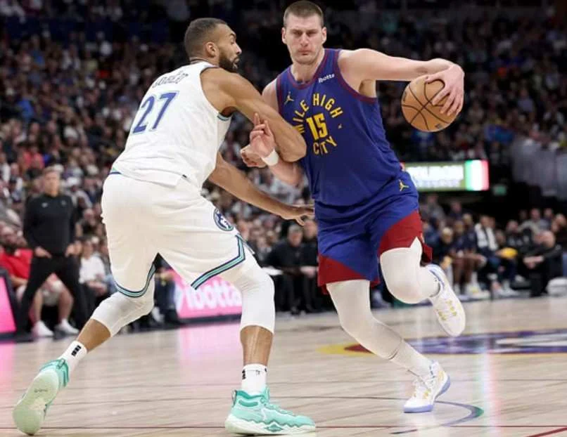 Two basketball players are engaged in a drill during a game, with one dribbling while the other defends.